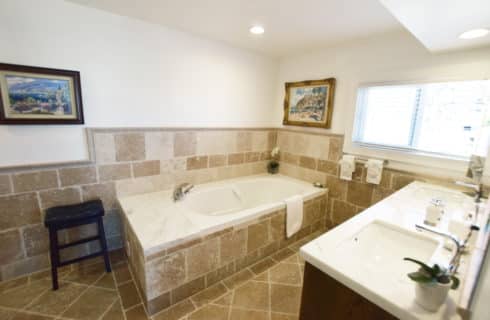 Bathroom with tan tiles on walls, floor, and tub with large double vanity with marble countertop