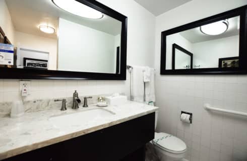 Bathroom with white-tiled wall, large mirror with dark wood frame, large vanity with granite countertop