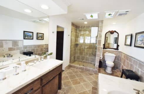 Bathroom with tan tiles on walls, floor, and tub with large double vanity with marble countertop