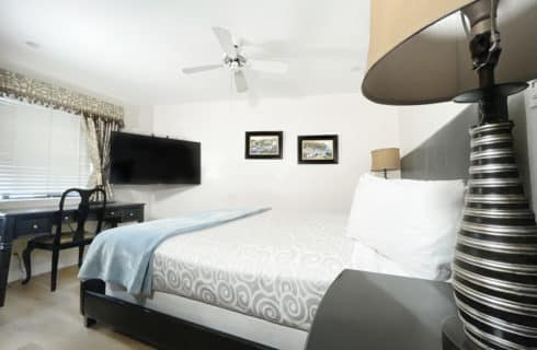Bedroom with dark wood furniture, black and gold lamps, flat-screen TV mounted on wall near window, and white ceiling fan