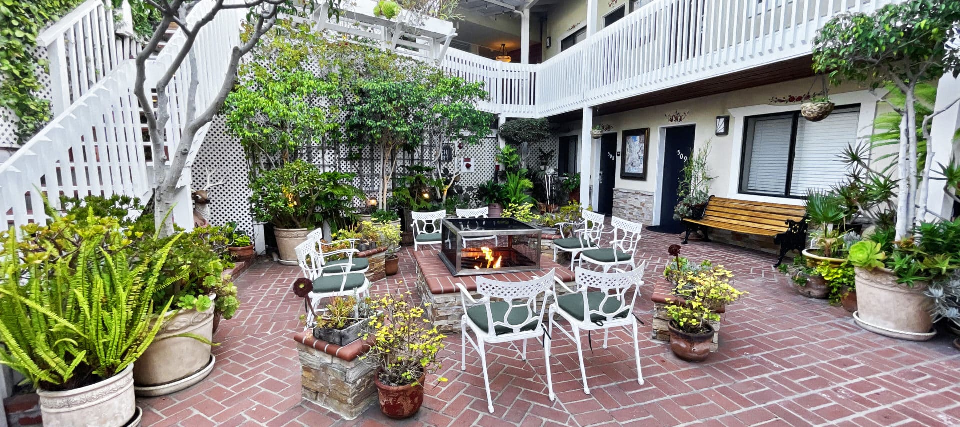 Courtyard patio with red brick and white chairs around a stone fire pit with greenery