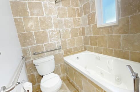 Bathroom with tiled walls, floor, and tub, large wooden vanity with small makeup table and granite countertops