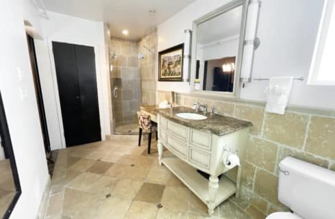 Bathroom with tiled walls, floor, and shower, large wooden vanity with small makeup table and granite countertops