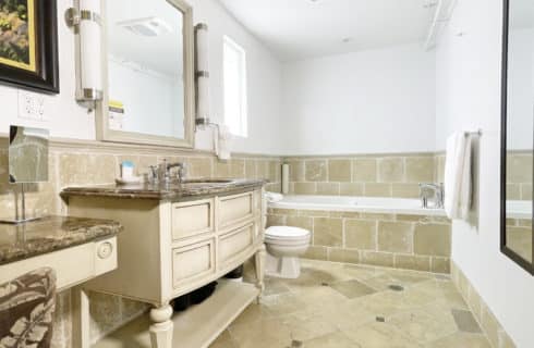 Bathroom with tiled walls, floor, and tub, large wooden vanity with small makeup table and granite countertops
