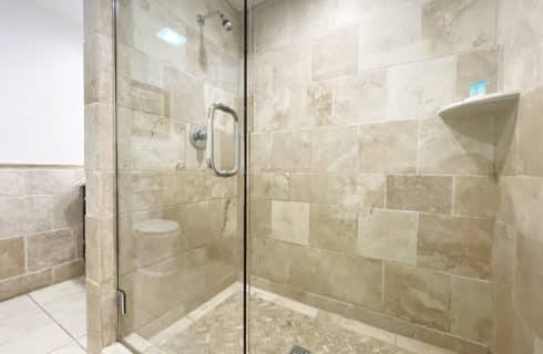 Bathroom with large shower with light tan tile on walls, floor, and tub with dark wood vanity and granite countertop