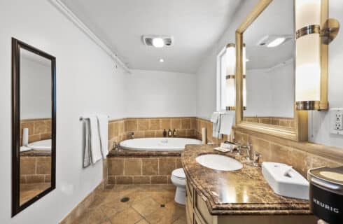 Vanity with toilet with tile foor and surround with vanity lights and white walls
