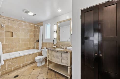 jetted tub with shower , toilet vanity and mirror with tile / tub surround same as flooring and entrance to closet.