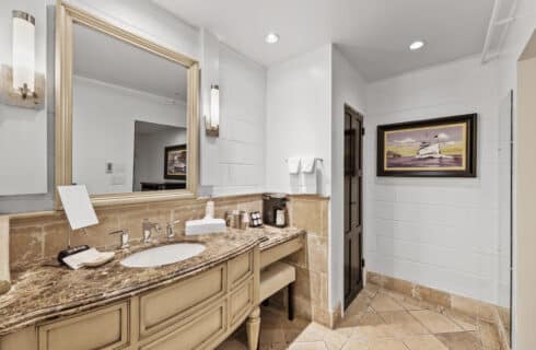 Vanity with marble counter, vanity miroor and artwork in the background with closet