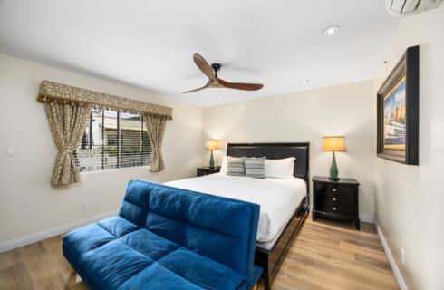 King bed with ceiling fan artwork on the wall. Blue sofa sleeper wood floors and black bed frame.