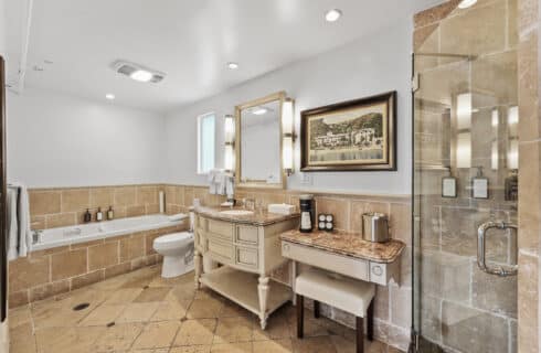 vanity, jetted tub, toilet with travertine fllor and surrounding with vanity and bench.