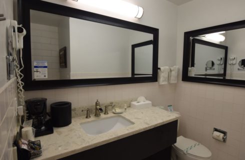 Bathroom with white-tiled wall, large mirror with dark wood frame, large vanity with granite countertop