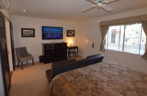 Bedroom with dark wood dresser and desk, dark brown leather couch, flat-screen TV mounted on wall, and white ceiling fan