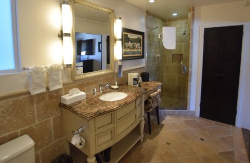 Bathroom with tiled walls, floor, and shower, large wooden vanity with small makeup table and granite countertops