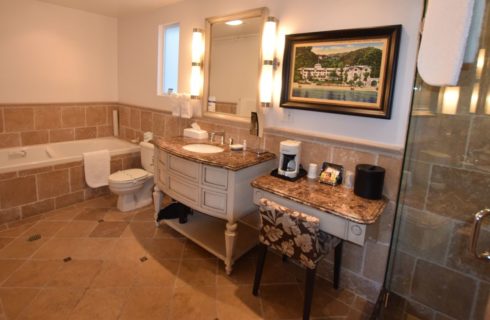 Bathroom with tiled walls, floor, and tub, large wooden vanity with small makeup table and granite countertops