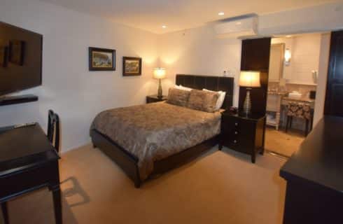 Bedroom with dark wood furniture, light brown bedding, large flat-screen TV mounted on wall