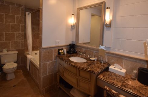 Light tan tiled bathroom and tub with wooden vanity and granite countertop