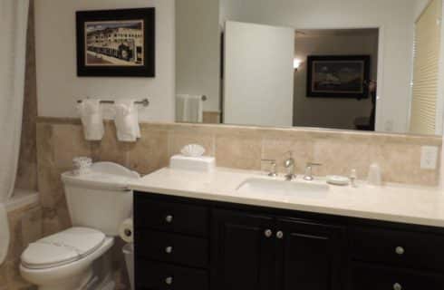 Bathroom with light tan tile on walls, floor, and tub with dark wood vanity and granite countertop