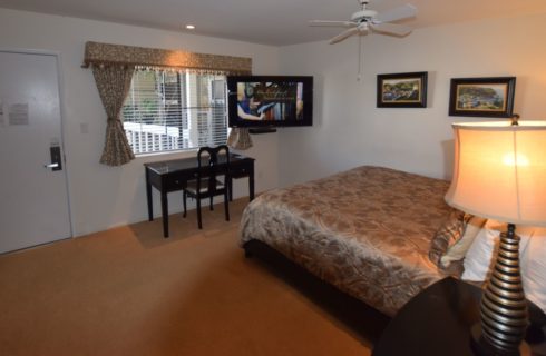 Bedroom with dark wood furniture, black and gold lamps, flat-screen TV mounted on wall near window, and white ceiling fan