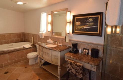 Bathroom with light tan tiled floors, tub, and walls with large vanity and granite counter tops