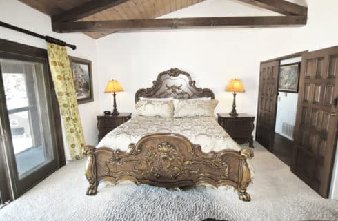 Bedroom with large ornate wooden bed with gold and cream bedding, ornate nightstands with dark wood lamps