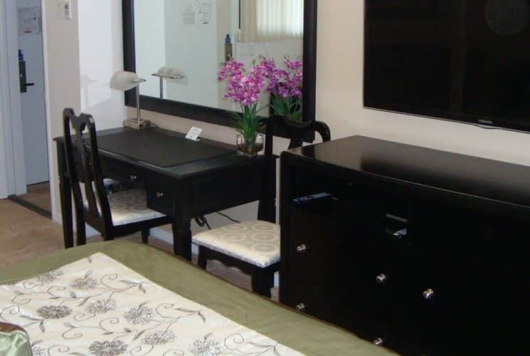 Bedroom with dark wood furniture, desk with two chairs, dresser, and large flat-screen TV