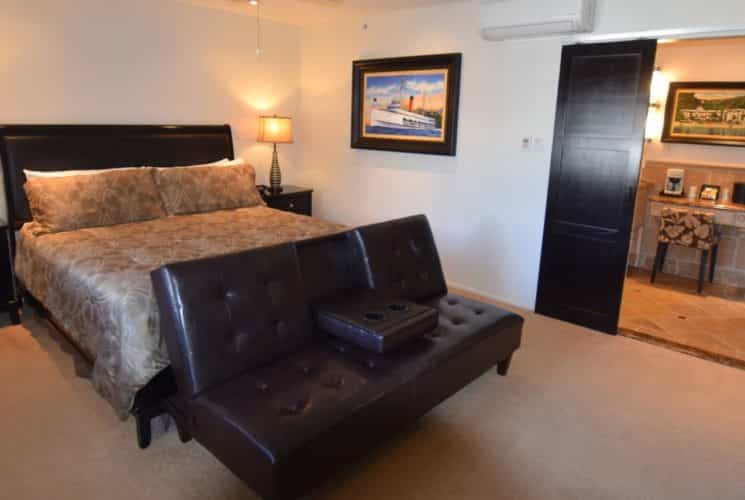 Bedroom with dark wood furniture, light tan bedding, black and gold lamps, and dark brown leather couch