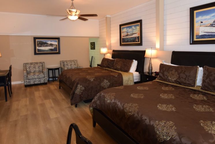 Large bedroom with dark brown furniture, two king beds with dark brown bedding, and two upholstered chairs