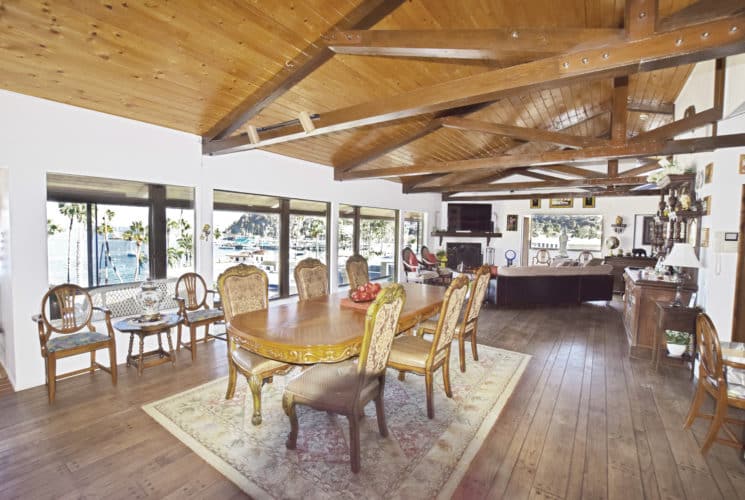 Very large living space with wood floor, ceiling, and beams including large ornate wooden dining table, sitting area, fireplace, and large flat-screen TV