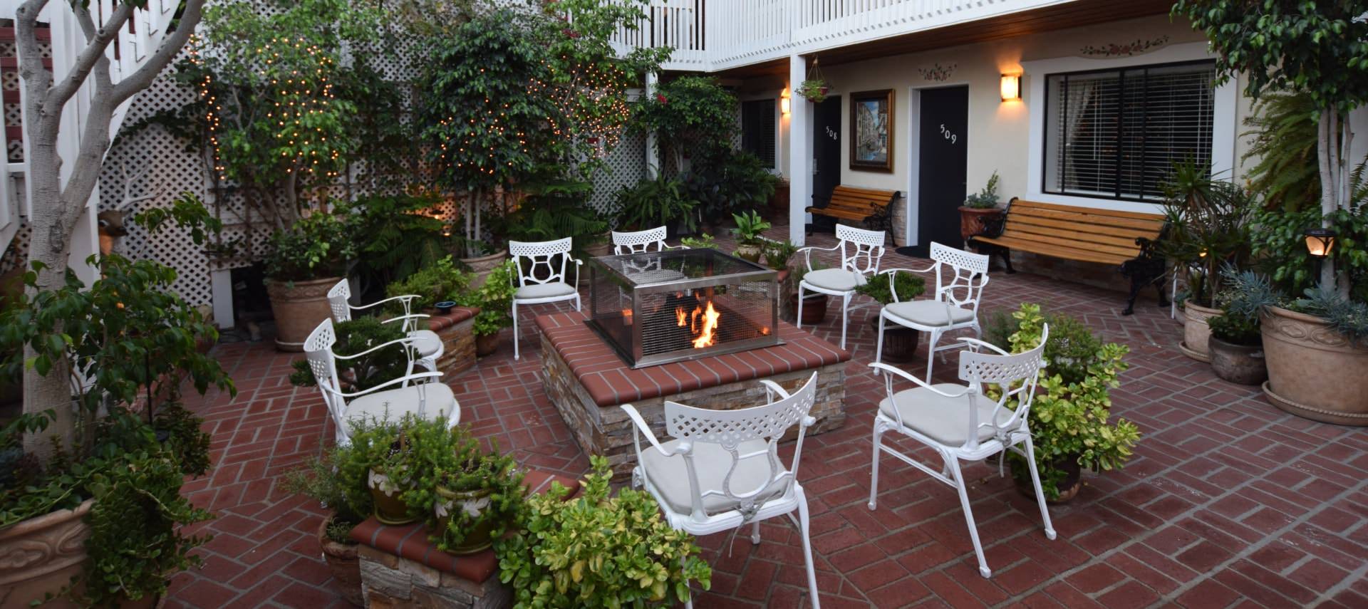 Courtyard patio with red brick and white chairs around a stone fire pit with greenery