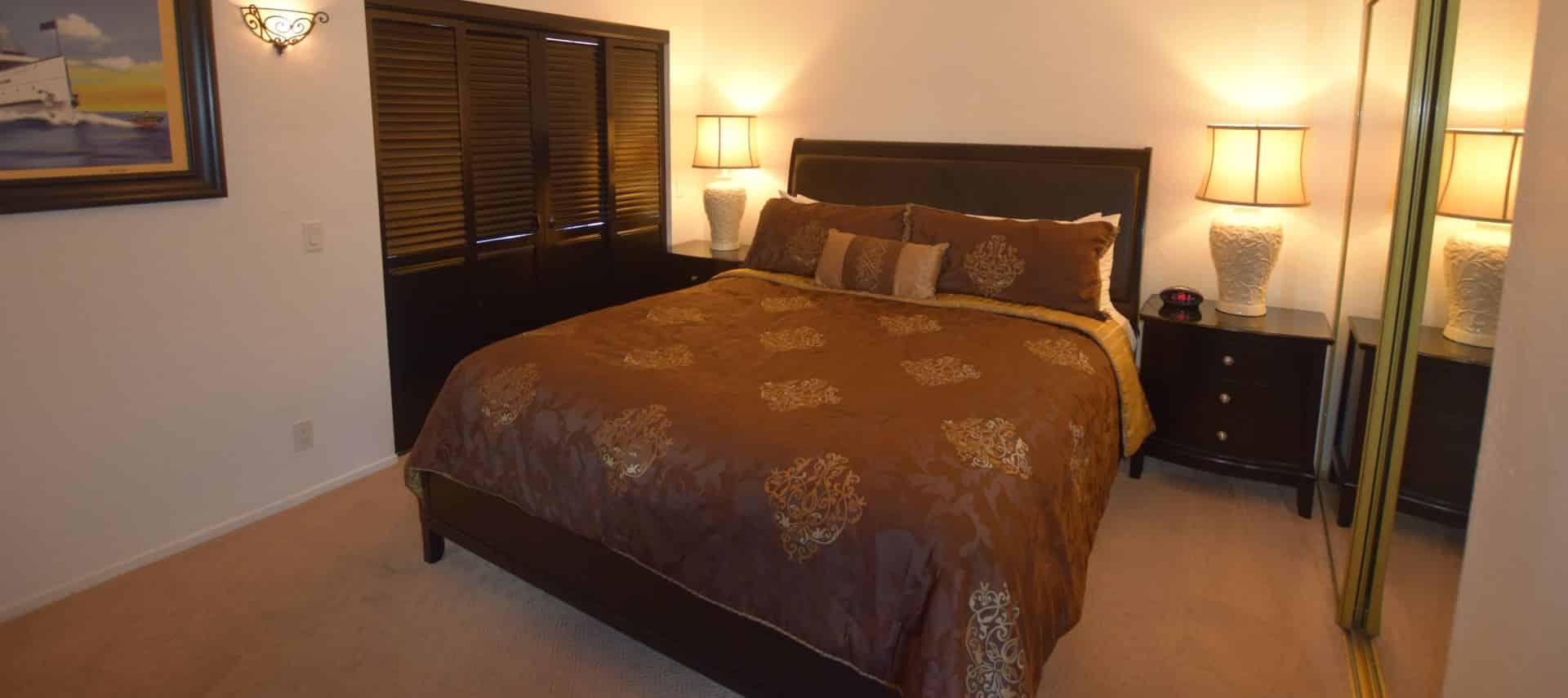 Dark wooden bed with brown and tan bedding with dark wood nightstands with white porcelain lamps